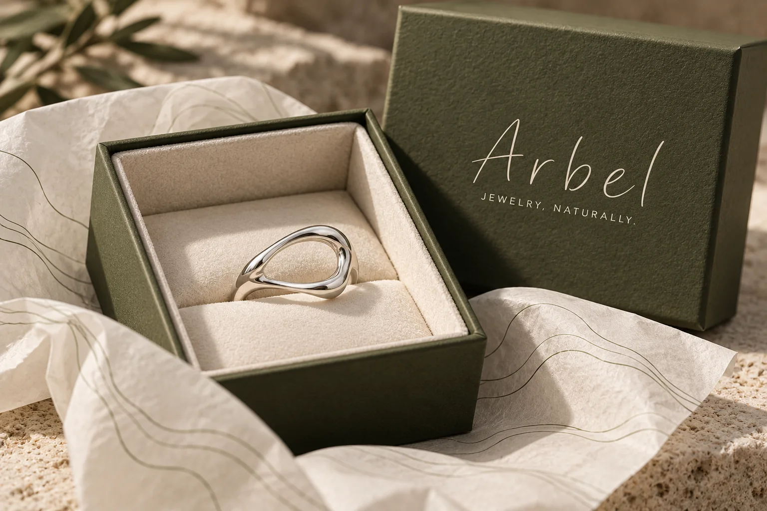 טבעת בגוון כסף בקופסה בצבע זית עם הלוגו של Arbel, על נייר עטיפה מודפס בקווי נוף דקים.